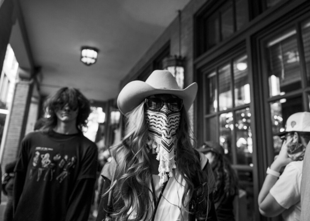 A masked protester walks on the sidewalk of Navarro at the Anacacho Coffee & Cantina during the “No Kings” protest Saturday. Photo by Jacob R. Lopez.