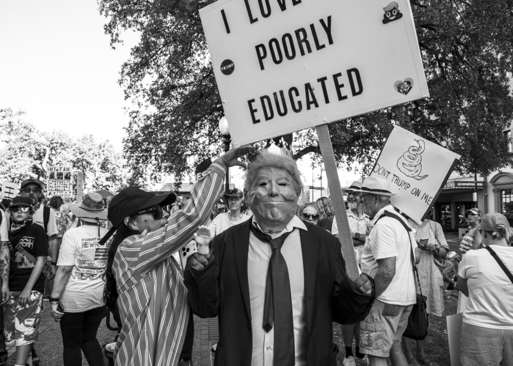 A protester dressed as President Donald J. Trump holds an “I Love the Poorly Educated” sign at Travis Park during the “No Kings” protest Saturday. Photo by Jacob R. Lopez.