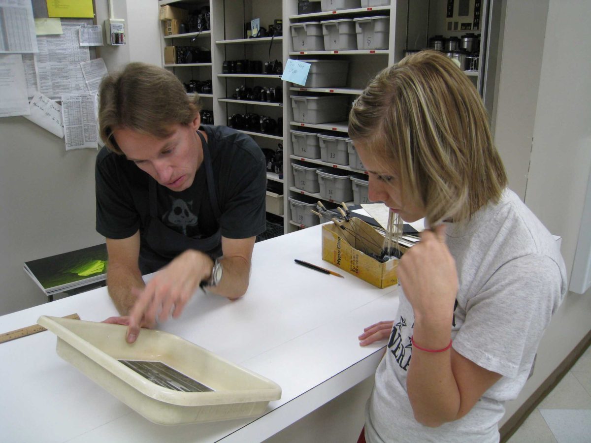 Photography Academic Lab Technician Mark Magavern goes over exposure and contrast with a student working in the black and white darkroom. Students used to expose their images and bring them out into the light to get direction on what to do to improve them. Archive photo.