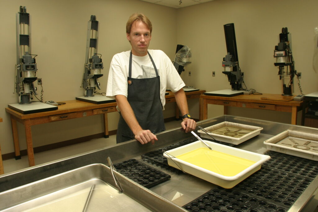 Photography Academic Lab Technician Mark Magavern stands in the photography dark room with 20 black-and-white photo enlargers. When the journalism program transitioned to digital photography, the room was converted to a smaller studio for table top illustrations. Archive photo.